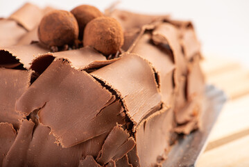 Chocolate cake, close-up of a chocolate cake decorated with curled chocolate shavings and dusted cocoa truffles on a silver tray over a rustic wooden surface, selective focus.