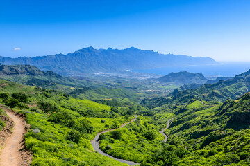 Naklejka premium Panoramic view of a winding road through lush green mountains and valleys, leading to a distant ocean under a clear blue sky