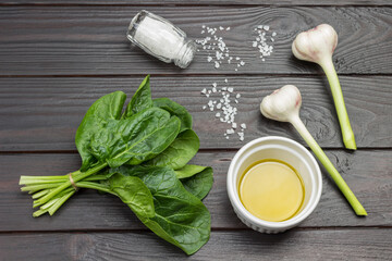 Spinach leaves are tied in bunch. Olive oil in white bowl.