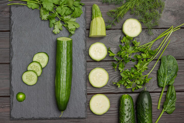 Sliced cucumber, cilantro on cutting board. Sliced zucchini, spinach and parsley on table