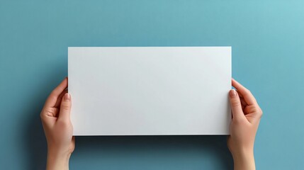 Hands holding blank white rectangular card against solid blue background for mockup.