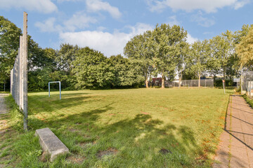 A serene park scene featuring lush greenery, a grassy field, and a football goalpost set against a blue sky with scattered clouds. Ideal for outdoor activities.