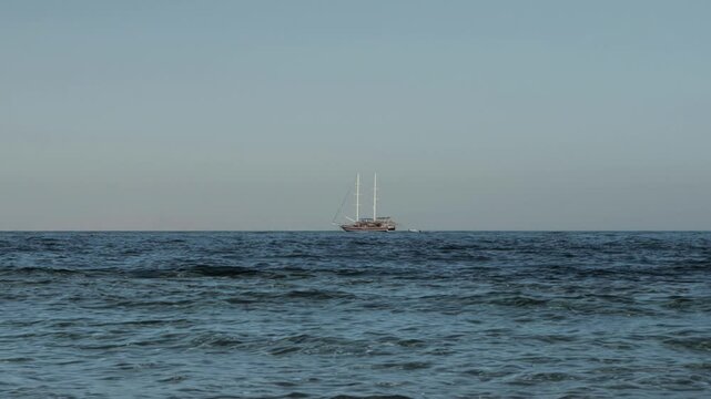 Two-masted sailing ship Brig with lowered sails floats on sea on horizon. Cruise holidays on tourist Brigantine vessel. Pure chill, concept of dream getaway. Extreme Long Wide Shot