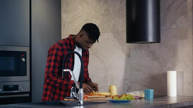 African American man preparing sandwich, adding cheese slices to bread