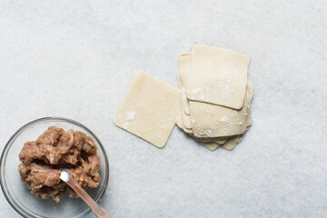 Overhead view of raw homemade wontons wrapper and filling on a white countertop, process of making...