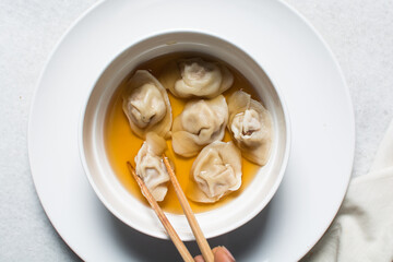 Overhead view of wonton soup in a white ceramic bowl, clear soup with dumplings in a white soup bowl