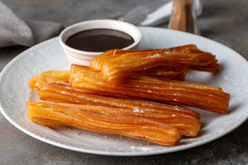 Traditional Spanish treat street fast food churros on a plate with hot chocolate sauce.