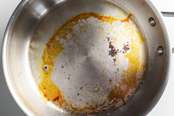 Burnt stainless frying pan on a white table. Top view