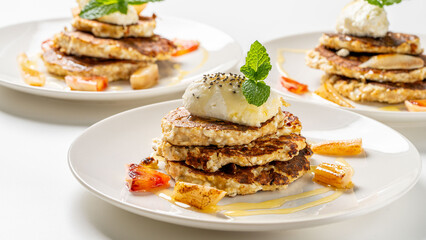 Healthy, dietary breakfast. Cottage cheese pancakes with cream cheese, orange, honey and mint on a white plate and background.