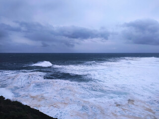 Dramatic ocean view under a stormy sky. Powerful waves crash against the shore, showcasing natures raw energy. Perfect for conveying themes of resilience, challenge, or solitude.
