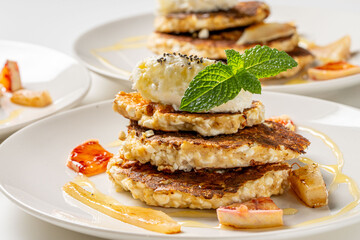 Cottage cheese pancakes with honey, orange, mint and cream are decorated with mint on a white plate. The concept of a delicious and healthy dietary breakfast. Close-up.