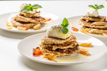 Cottage cheese pancakes with honey, orange, mint and cream are decorated with mint on a white plate. The concept of a delicious and healthy dietary breakfast. Close-up.