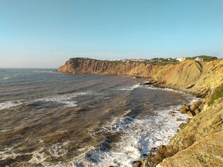 Coastal cliff view of rough waves crashing against the rocks in the afternoon sunlight at a scenic seaside location