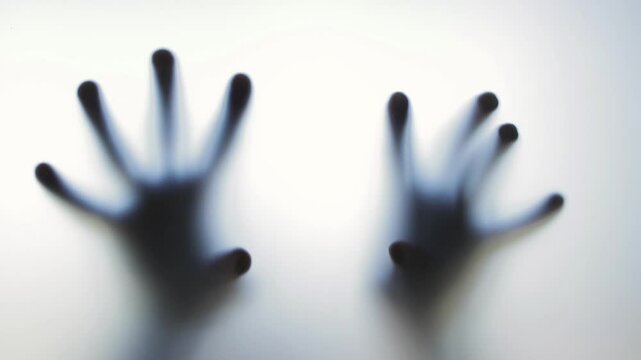 Blurred, ghostly hands pressing and sliding along frosted glass surface, creating mysterious shadowy interaction against white background