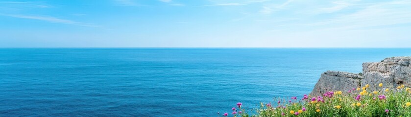 Obraz premium Vibrant Wildflowers Blooming on a Majestic Cliffside Overlooking the Expansive Ocean with a Clear Blue Sky Creating a Tranquil Scenic Viewpoint