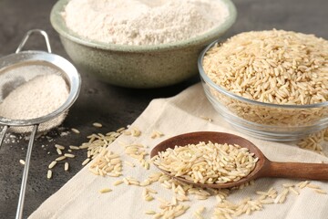 Brown rice, flour and sieve on grey table, closeup