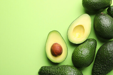 Whole and cut avocados on light green background, flat lay. Space for text