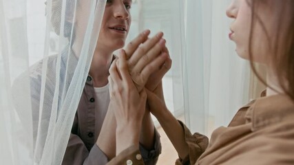 Tilt-down shot of affectionate couple holding hands and being silly, standing near window at home