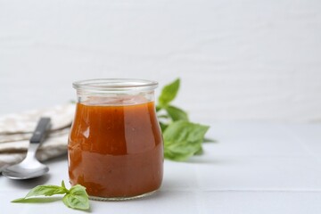 Tasty curry sauce in glass jar and basil on white tiled table, closeup. Space for text