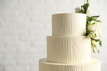 Delicious wedding cake decorated with flowers near white brick wall, closeup. Space for text