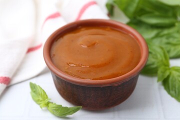 Tasty curry sauce and basil leaves on white tiled table, closeup
