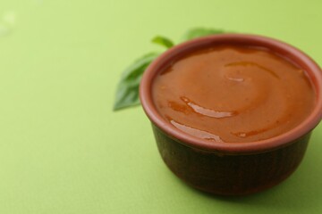 Tasty curry sauce and basil leaves on green background, closeup. Space for text