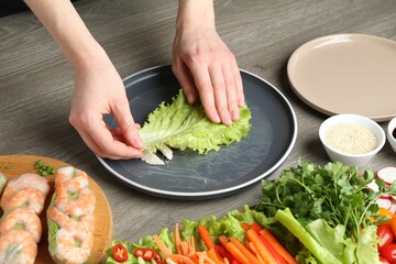Woman making tasty spring roll at grey wooden table, closeup