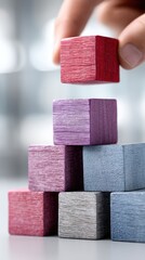 Hands adding wooden blocks in red and purple to a tower on an office table, symbolizing business growth and strategy