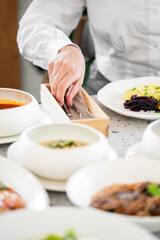 A close-up of a person's hand reaching for utensils from a wooden holder, surrounded by a variety of delicious dishes, creating an inviting dining atmosphere.