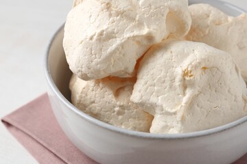 Delicious homemade meringue cookies in bowl on light table, closeup
