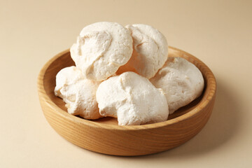 Delicious homemade meringue cookies in bowl on beige background, closeup