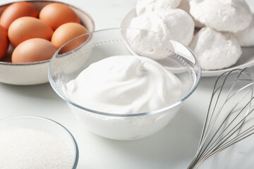 Whisk, whipped cream in bowl and other ingredients on light table, closeup. Cooking meringue cookies