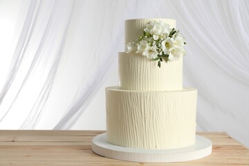 Delicious wedding cake with floral decor on wooden table and curtains against white background,...