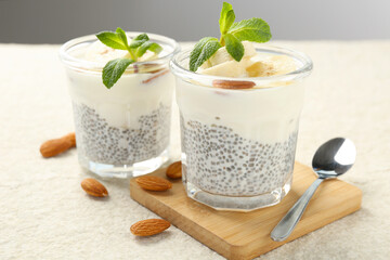 Delicious dessert with chia seeds, yogurt, banana, almond and mint in glasses on light textured table, closeup. Superfood