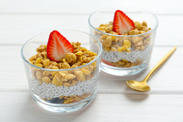 Delicious dessert with chia seeds, yogurt, granola and strawberries in glasses on white wooden table, closeup. Superfood