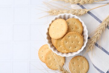 Tasty salty crackers with wheat spikes on white tiled table, flat lay. Space for text