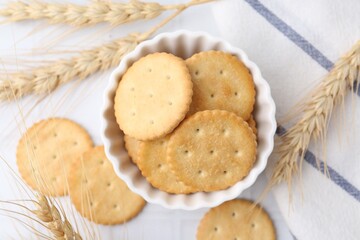 Tasty salty crackers with wheat spikes on white tiled table, flat lay