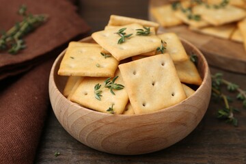 Tasty salty crackers with thyme on wooden table, closeup
