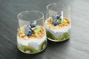Delicious dessert with chia seeds, yogurt, granola, blueberries and kiwi in glasses on grey table, closeup. Superfood