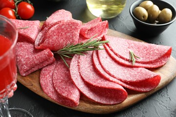 Slices of delicious sausage with rosemary served on black table, closeup