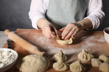 Woman making khinkali on table in kitchen, closeup