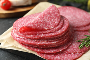 Slices of tasty smoked sausage and rosemary on black table, closeup