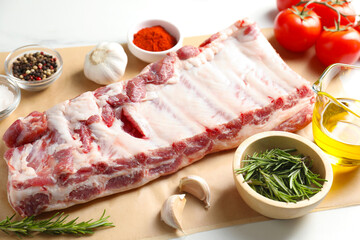Raw pork ribs, spices and tomatoes on white table, closeup