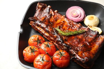 Delicious roasted pork ribs with rosemary, tomatoes and onions on light table, closeup