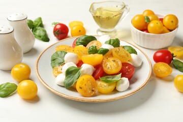 Fresh salad with yellow tomatoes, basil and mozzarella cheese on white marble table, closeup