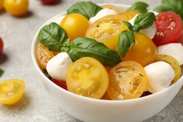 Fresh salad with yellow tomatoes, basil and mozzarella cheese on grey table, closeup
