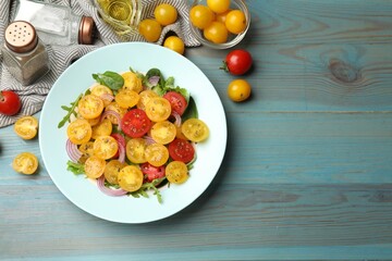 Fresh salad with yellow tomatoes served on light blue wooden table, flat lay. Space for text