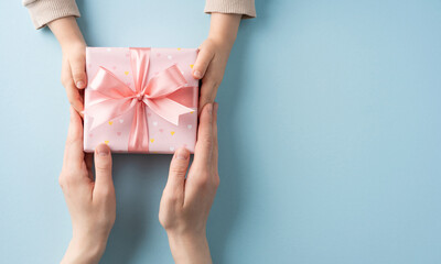 Child's hands offering a pink present with ribbon to an adult, symbolizing giving