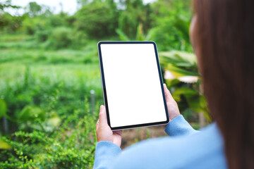 Mockup image of a woman holding digital tablet with blank white desktop screen in the nature outdoors