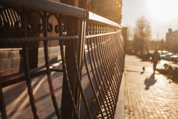 City scene. Metal railing glowing in warm sunset light with a city sidewalk in the background....